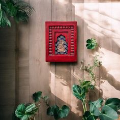 a wooden wall with plants and a small red frame on the wall, in front of it