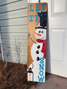 a wooden sign that says let it snow on the side of a house with a snowman