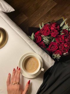 a woman's hand with red nails next to a cup of coffee and bouquet of roses