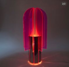 a pink lamp sitting on top of a table next to a black vase with a red light in it