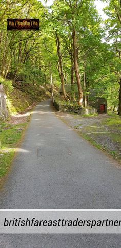 an empty road in the middle of a forest with trees on both sides and a sign above it that says british fasttraderspartners