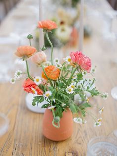 an arrangement of flowers in a vase sitting on a wooden table with white and orange napkins