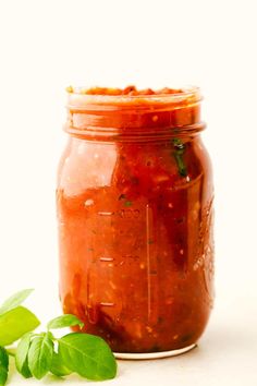 a jar filled with tomato sauce and basil leaves