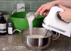 a person pouring something into a bowl on top of a counter next to a mixer