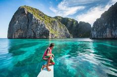 a person sitting on the end of a boat in clear blue water next to an island