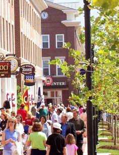 many people are walking down the sidewalk in front of shops and restaurants on a sunny day