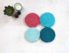 four crocheted coasters sitting next to a candle