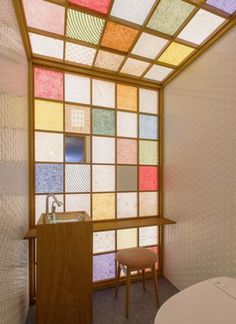 a toilet sitting next to a window covered in multicolored glass tiles on the wall