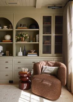 a brown chair sitting in front of a book shelf filled with books and vases