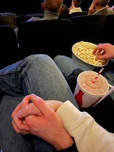 two people are sitting on the couch eating popcorn and drinking soda while watching movies together