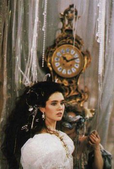 a woman in a white dress standing next to a clock