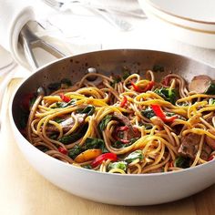 a pan filled with noodles and vegetables on top of a wooden table