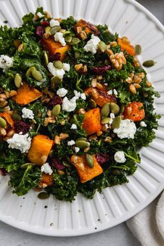 a white plate topped with kale salad and feta cheese covered in nuts, pumpkins and cranberries