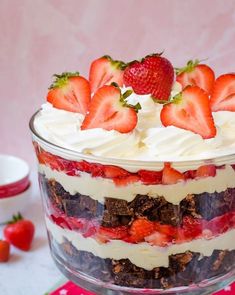 a layered dessert with strawberries and chocolate in a glass dish on a red place mat