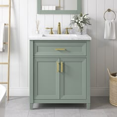 a bathroom with white walls and gray flooring has a green cabinet, gold handles on the door