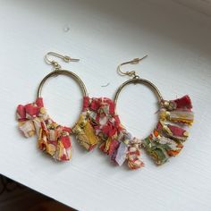 two pairs of colorful fabric earrings hanging from hooks on a white surface with wood planks