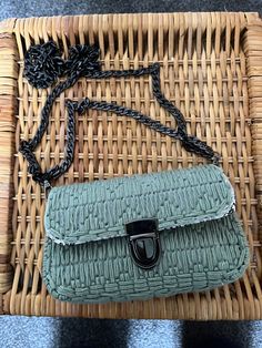 a green purse sitting on top of a wicker basket next to a black chain