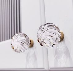 a pair of glass knobs on a white cabinet with gold handles and pulls in the shape of a leaf