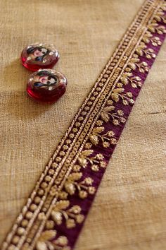 Wine and gold - a colour combination that spells royalty. This elegant trim displays a row of little flowers in gold. It is created with gold zari embroidery on a wine cotton silk fabric. Embellished with tiny sequins. Regal and unique, will add a dash of glamour to anything it touches. Use it to embellish your denim jackets, or border your sarees. Or create home décor like lamps or curtain ties. Or accessories like hair bands. One trim, countless possibilities. Price for 1 mtr Size - 3.5 cm W N Gold Art Silk Embroidered Fabric For Festivals, Gold Silk Thread Choli For Eid, Traditional Gold Embroidered Raw Silk Fabric, Gold Silk Thread Embroidered Fabric For Diwali, Gold Embroidered Fabric For Ceremonial Festivals, Ceremonial Gold Embroidered Fabric For Festivals, Traditional Gold Silk Thread Choli, Gold Embroidered Raw Silk Choli, Gold Silk Thread Choli In Traditional Style