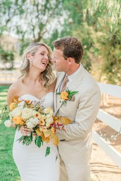 a bride and groom standing in front of a white fence