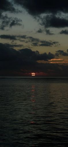 the sun is setting over the ocean with dark clouds in the sky and water below