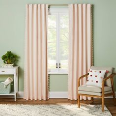 a living room with green walls and pink curtains on the window sill, white chair and rug