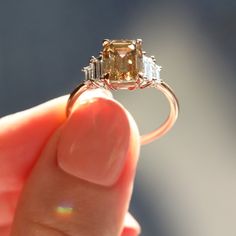 a person holding an engagement ring with two diamonds on the side and one diamond in the middle