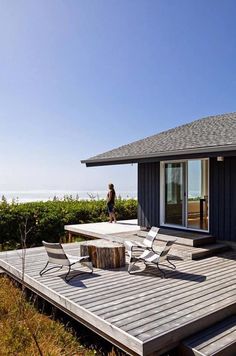 a woman walking on a deck next to a house with a table and chairs in front of it