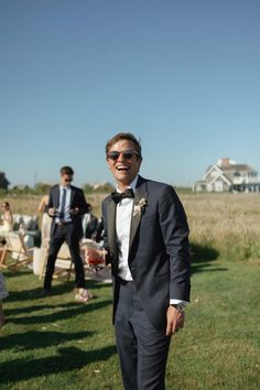 a man in a tuxedo smiles as he walks through the grass with other people