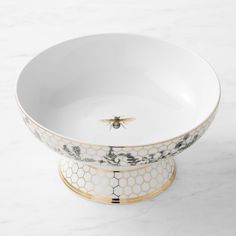 a white and gold bowl with a bee on the side sitting on a marble surface