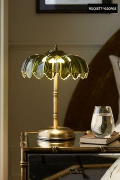 a table lamp sitting on top of a night stand next to a glass filled with water