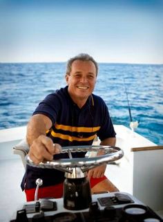 a man sitting at the helm of a boat smiling and holding onto his steering wheel