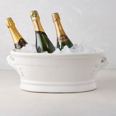 three bottles of champagne in a white bowl with ice on the bottom and gold trimmings