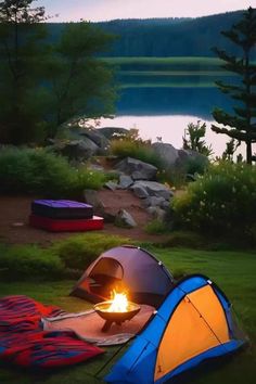 two tents set up next to each other on the grass near a lake with trees in the background