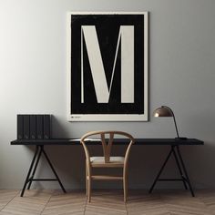 a desk with a chair next to it in front of a large black and white letter