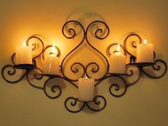 a wall mounted candle holder with five lit candles on it's sides and an iron scroll design