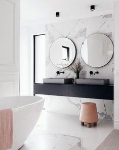 a bathroom with marble walls and floor, two round mirrors on the wall above the bathtub