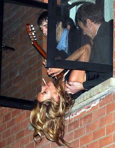 a woman holding a guitar in front of a window with other people looking out the window