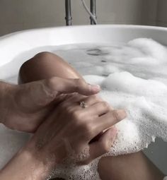 a woman is sitting in the bathtub with foam on her feet and holding onto her hand