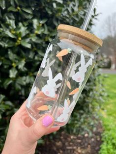 a person holding up a glass jar with some bunny designs on it and a straw lid