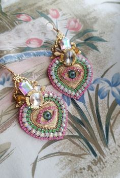 two pairs of colorful earrings on top of a flowered table cloth with flowers in the background