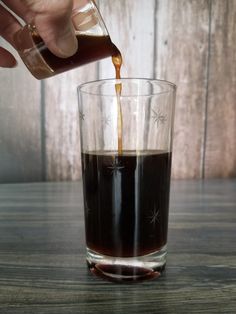 someone pouring coffee into a glass on top of a wooden table