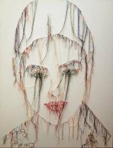 a drawing of a man's face is made out of colored threads on a white wall