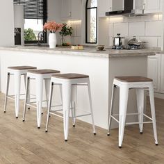 three white stools in front of a kitchen island with flowers on the counter top