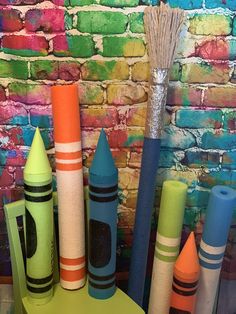 colorful crayons are lined up in front of a brick wall with a broom