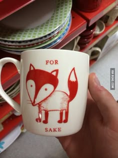 a hand holding a coffee mug with a red fox on it