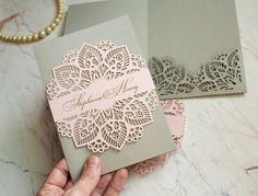 a person holding two wedding cards in their hands, one is pink and the other is gray