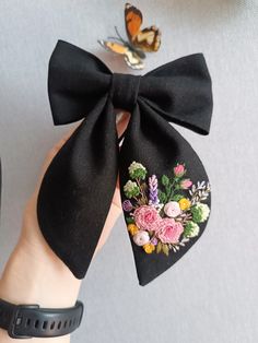 a woman's hand holding a black bow with flowers and butterflies on the side