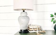 a white lamp sitting on top of a table next to a green vase and books