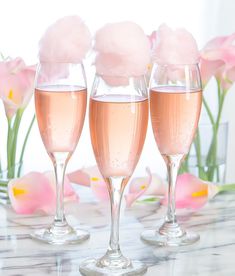 three wine glasses filled with pink liquid sitting on a table next to flowers and tulips